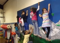   Children climbing on the rock wall inside the gym at Kiddie Company Enrichment Center.  