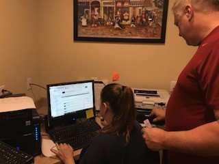 Working from home for a few hours, Kathleen LaGore uploads pictures of inventory to the business’s eBay page, while Chip LaGore works to fix a broken printer, that will later be displayed on eBay.