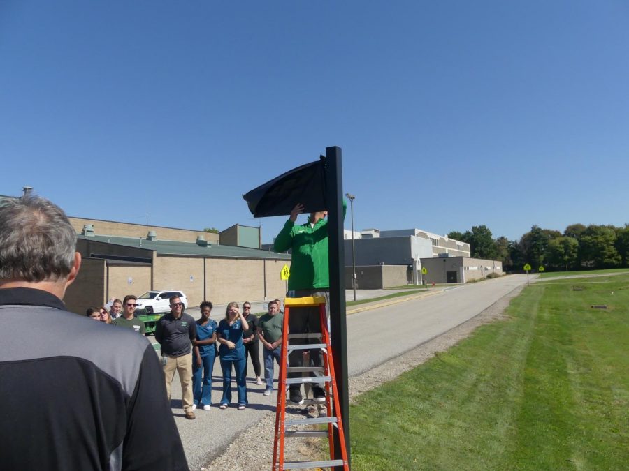 Athletic director Keith Leffler removes the cover from the new Stevie street sign behind the school.  Assistant principal Brian Linn, the swim team, and other members of the community were there for the reveal as well.